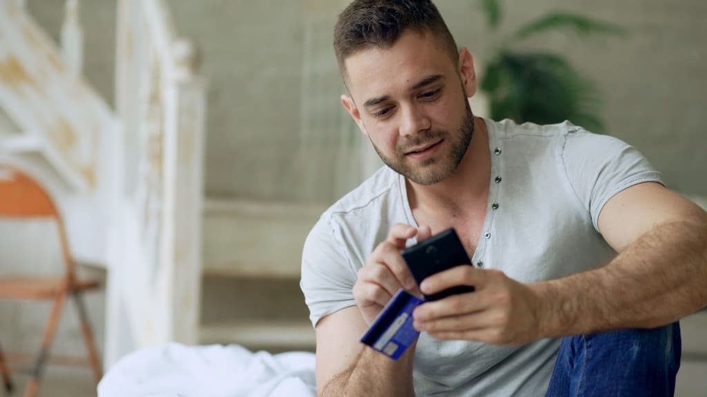 Person holding a credit card while checking a smartphone indoors